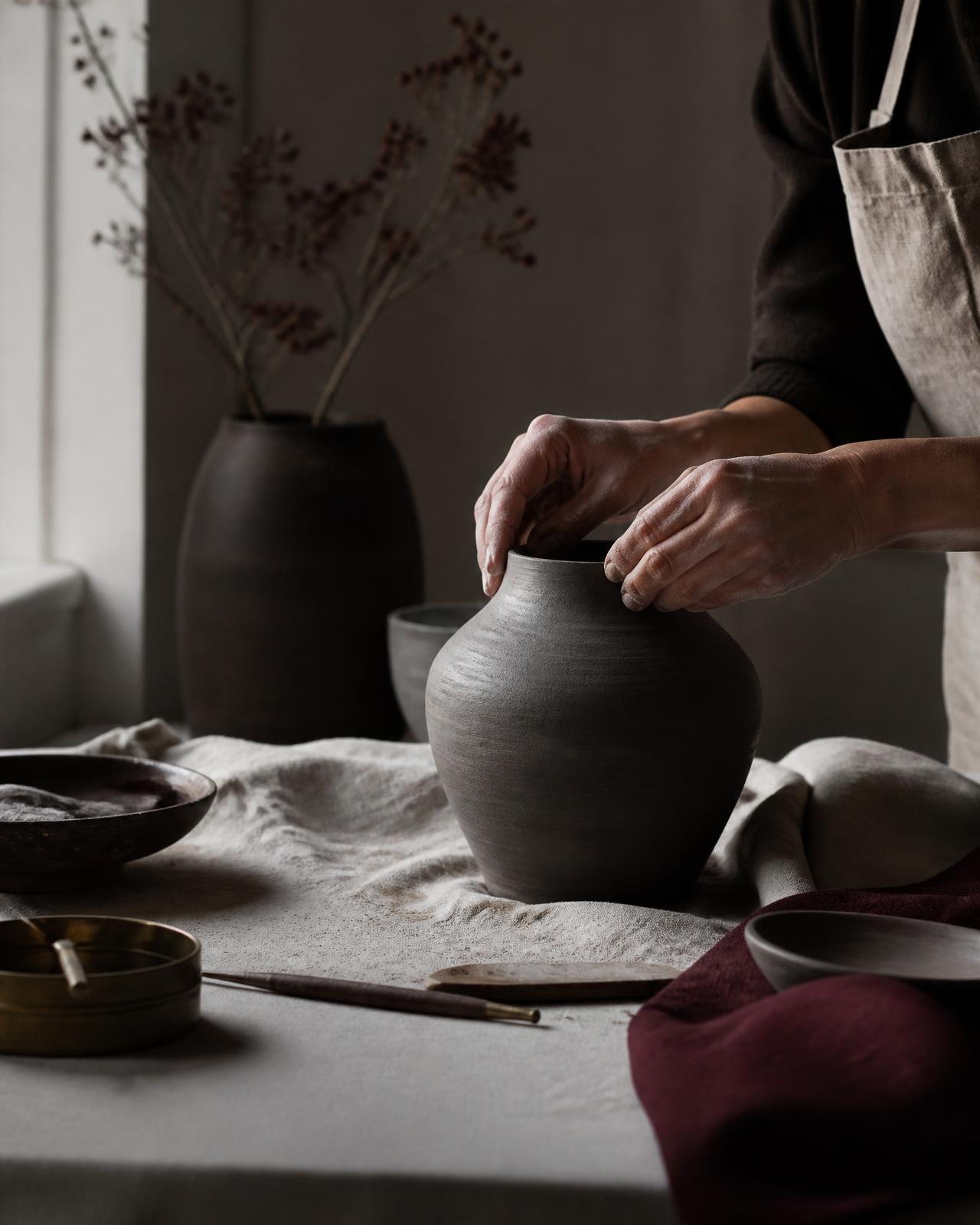 Artisan shaping a charcoal ceramic vessel by hand